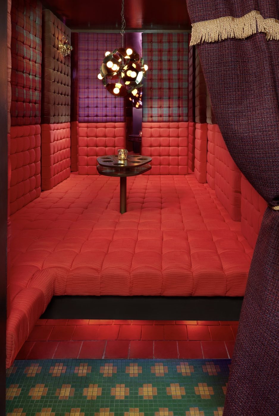 The Love Pit at HiLot — a private padded room with red velvet quilted walls and floor, tiled entry, and a hanging bulb-cluster chandelier